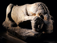 Stone sculpture of a lying lion with a human figure in its front paws and mouth
